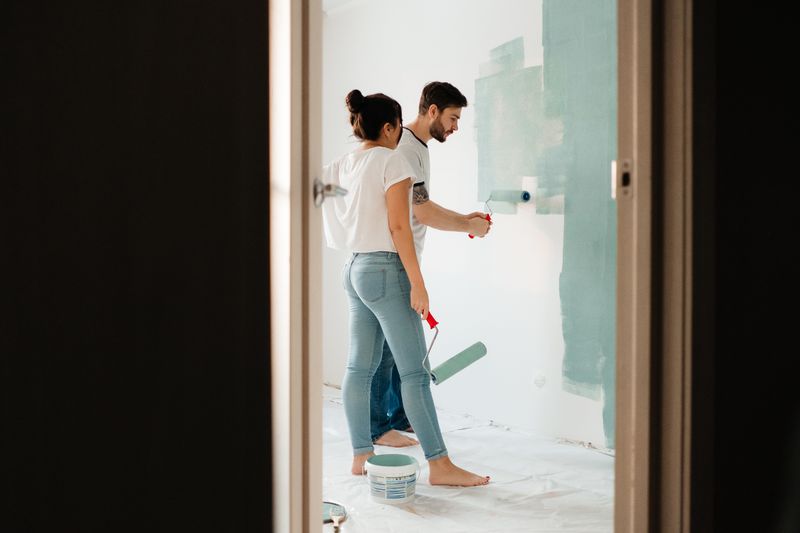A man and woman painting a room wall with rollers, showcasing teamwork in home renovation projects.