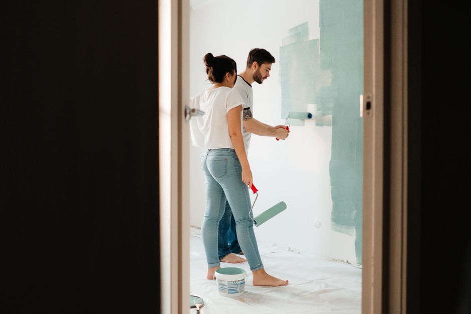 A man and woman painting a room wall with rollers, showcasing teamwork in home renovation projects.