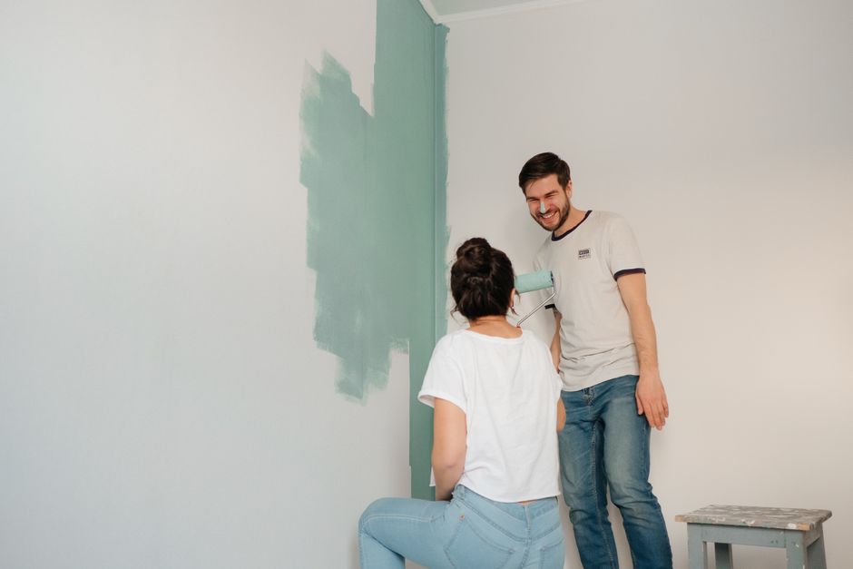 A couple laughing and enjoying painting a room together with a teal color.