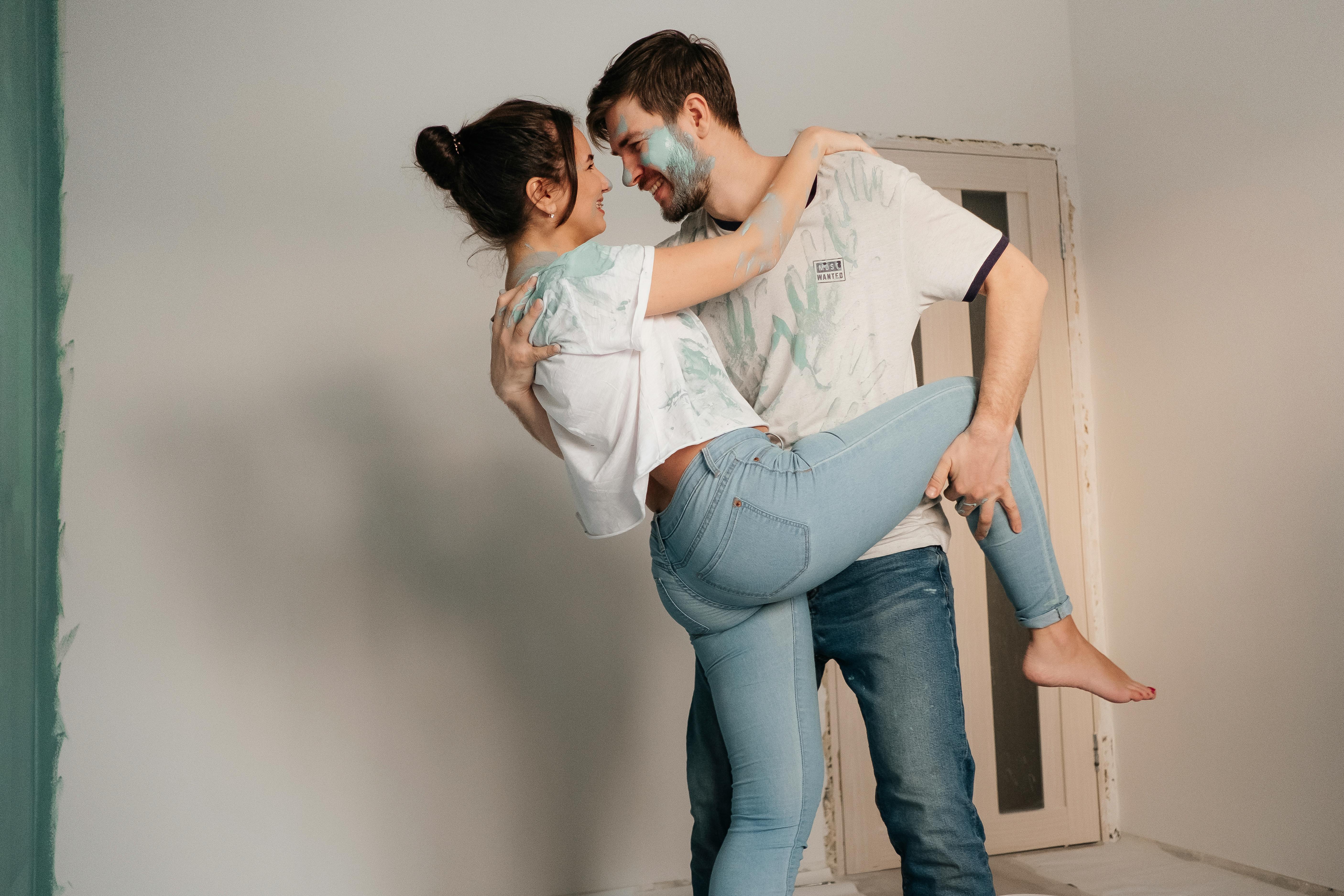 A joyful couple covered in paint, embracing while renovating their home indoors.