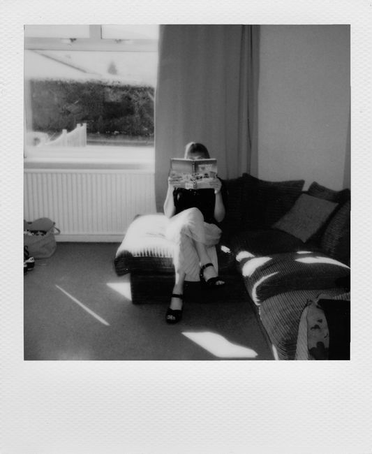 Black and white photo of a person reading on a sofa by a sunny window, creating a cozy atmosphere.