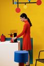 Woman in Orange Long Sleeve Dress Standing Beside White Table