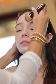 A woman receiving makeup with a brush applied by a skilled artist.