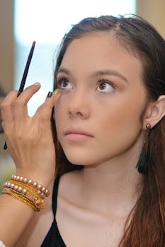 A makeup artist applies eyeliner to a young woman in a professional setting.