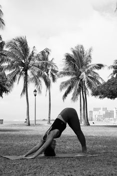Black and white photo of a woman doing yoga outdoors near palm trees.