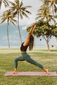 Woman in activewear performing yoga on a mat in a tropical park with palm trees.