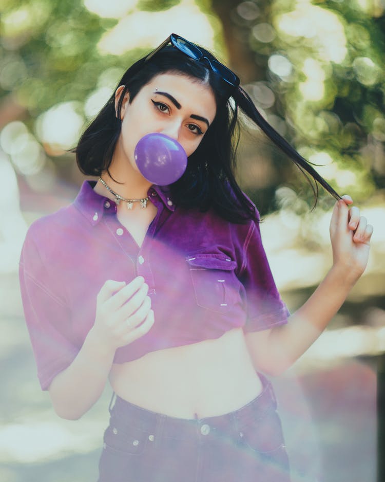 Young Woman Blowing Purple Bubble Gum In Park