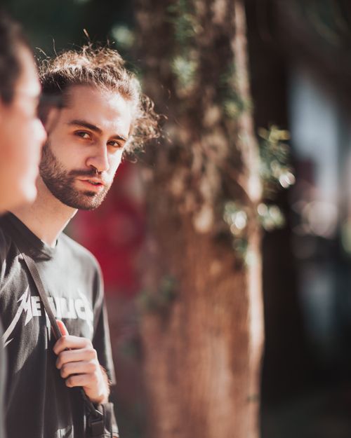 Free Concentrated young bearded guy in casual outfit looking at camera while walking on city street with crop unrecognizable male friend Stock Photo