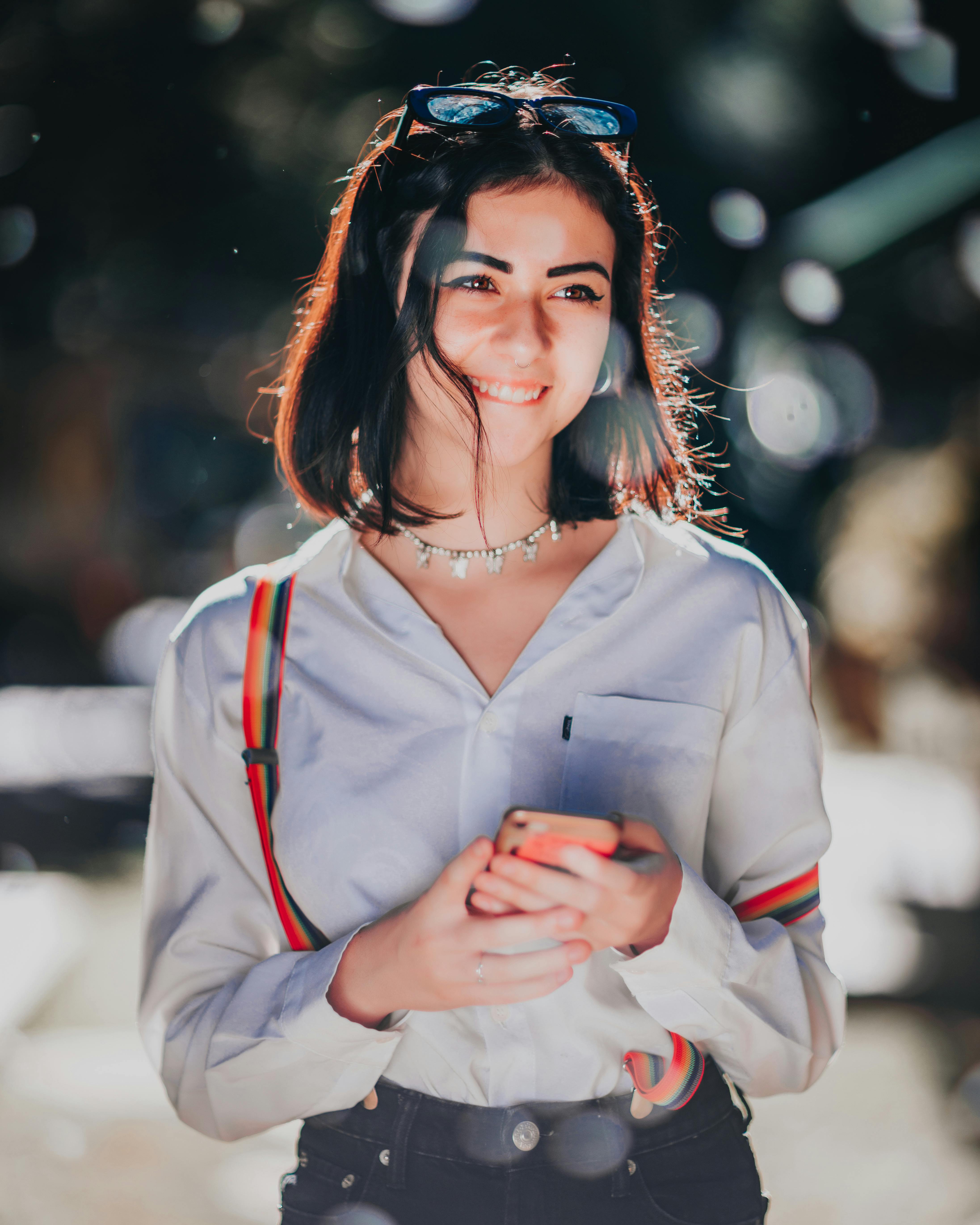 happy ethnic female teenager messaging on smartphone and smiling on street