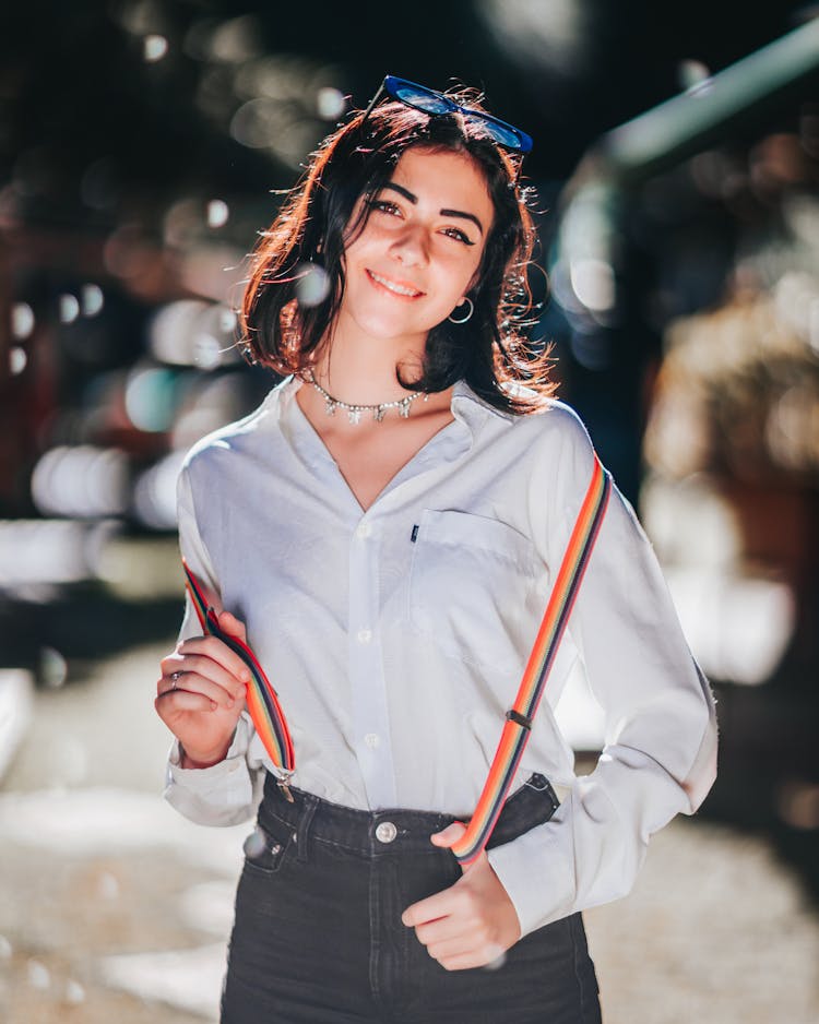 Positive Ethnic Teen Female Smiling And Adjusting Suspender On Street