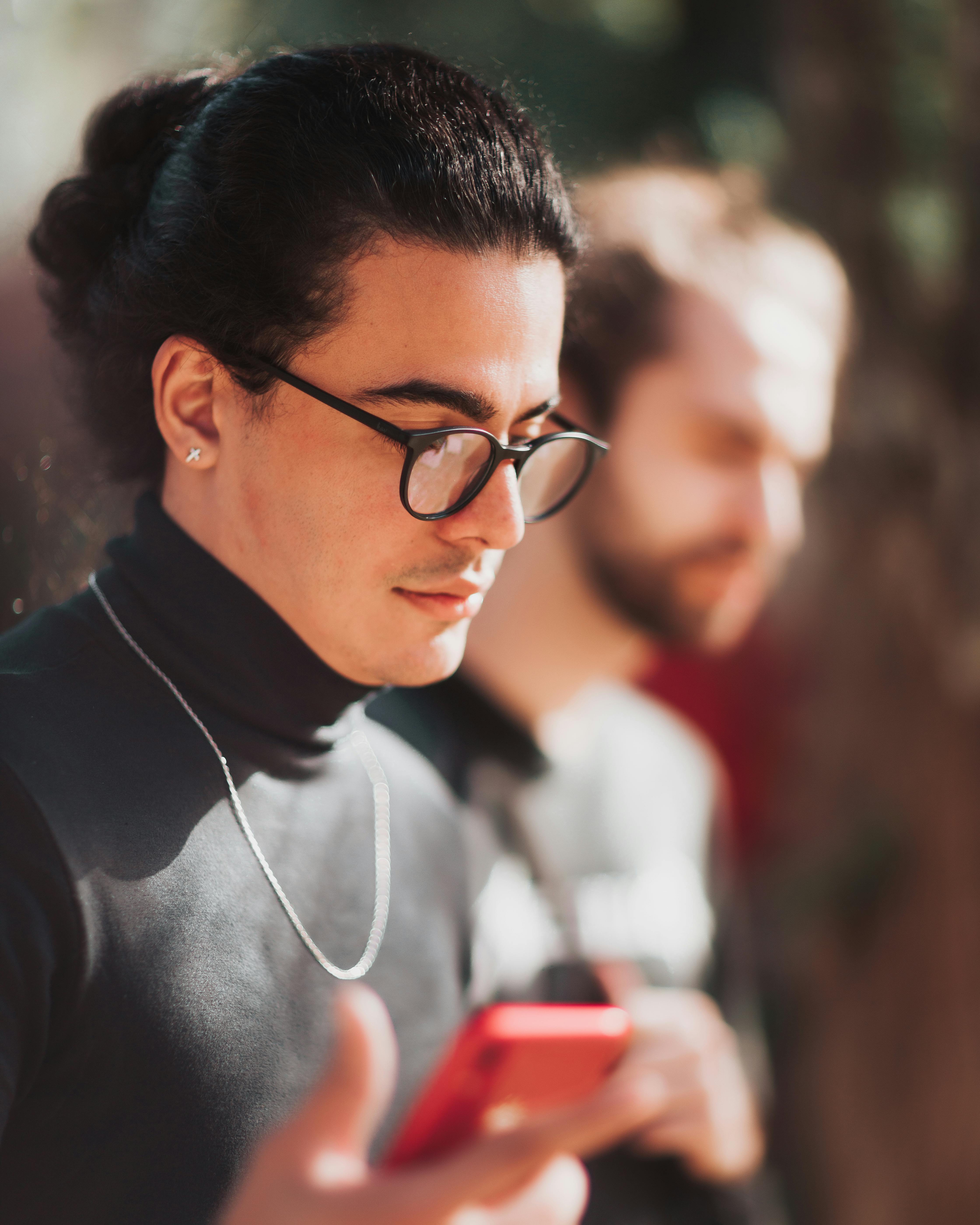 serious young stylish hispanic man using smartphone on street in sunlight