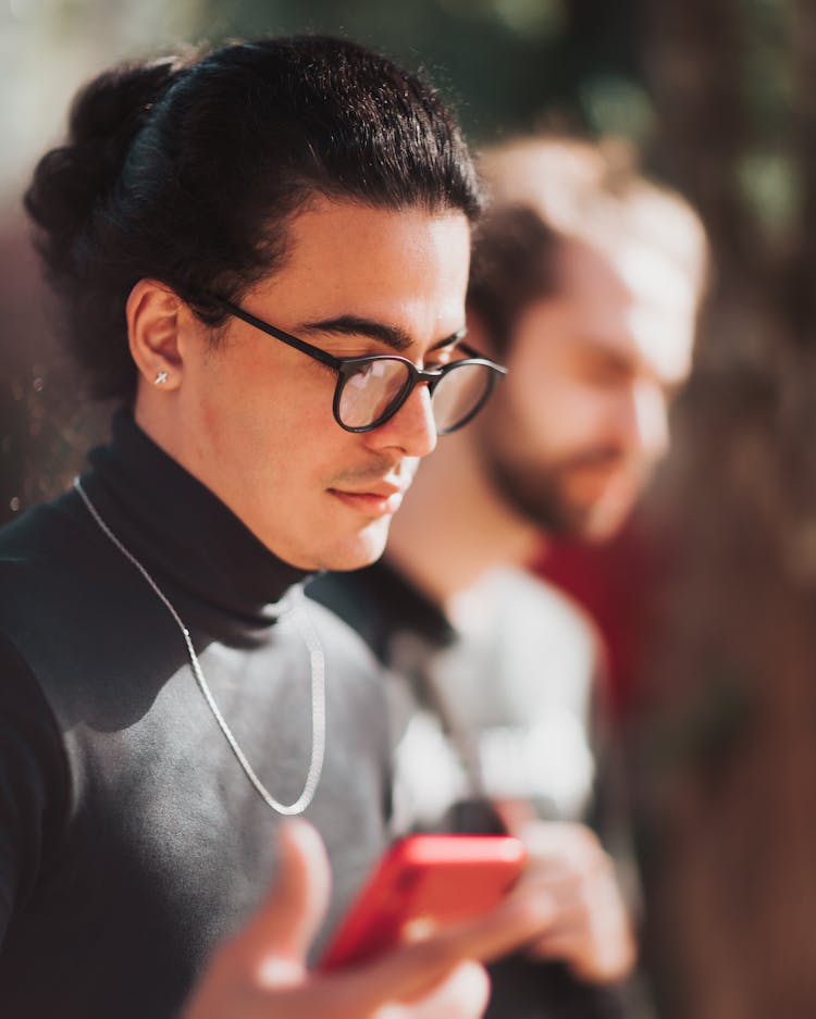 Serious Young Stylish Hispanic Man Using Smartphone On Street In Sunlight