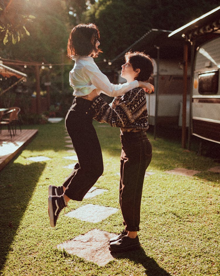 Trendy Female Teenager Supporting Friend Jumping On Lawn