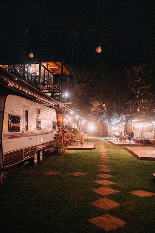White camping trailers parked under roof with glass balcony on street with streetlight and walkways at summer night