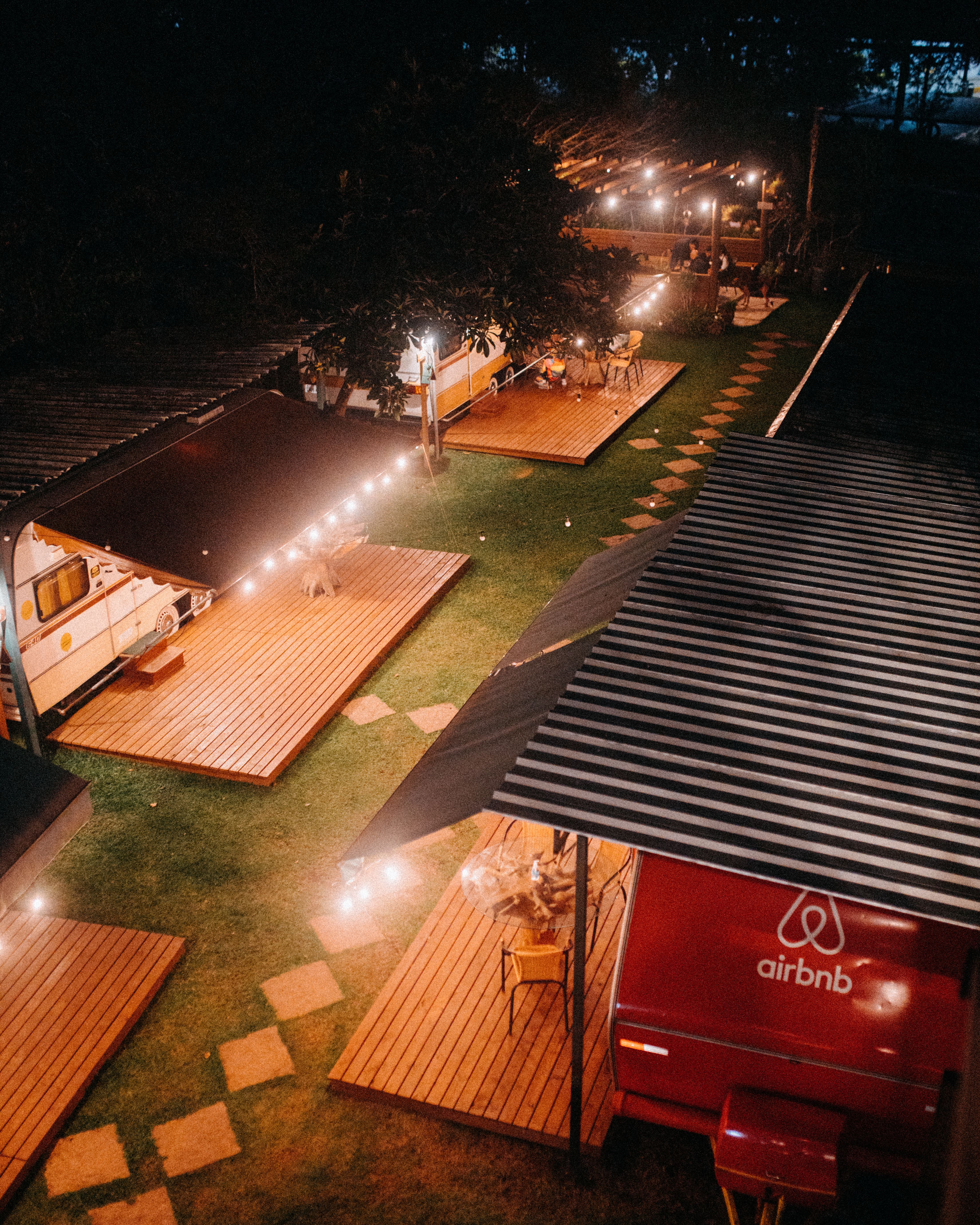 Fotomural Una vista aérea de un área de camping iluminada, con caravanas y plataformas de madera creando una atmósfera cálida.