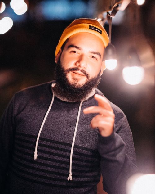 Free Adult hipster male in knitted hat and hoodie looking at camera against bright lights at night Stock Photo
