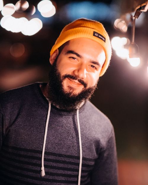 Free Cheerful adult bearded male in knitted hat looking at camera against shiny light bulbs in twilight Stock Photo