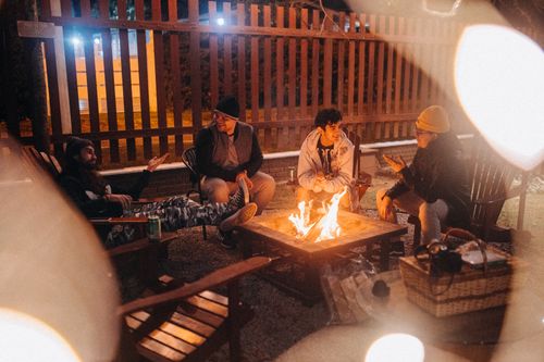 Free Cheerful male friends conversing against shiny flame while sitting in armchairs and looking at each other in campsite at dusk Stock Photo