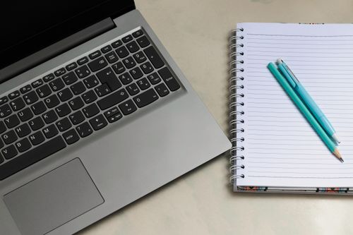 Free A close-up of a laptop and a notebook with a pencil and pen on a desk, perfect for work or study themes. Stock Photo
