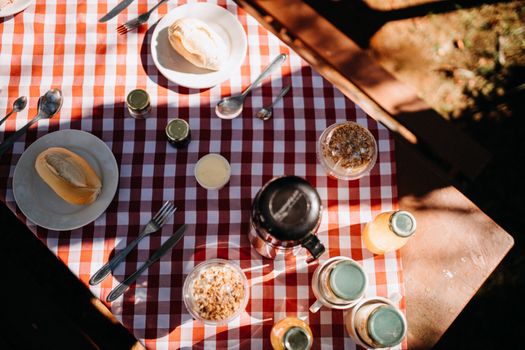 Top view composition of fresh buns on plates placed on tablecloth with thermos and juice during picnic on sunny summer day