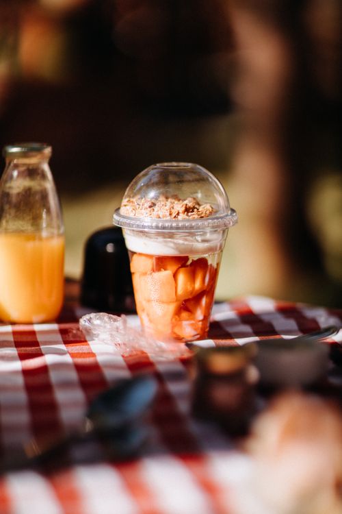Free Plastic cup filled with cut fresh fruits topped with yogurt and granola placed on table during picnic on blurred background Stock Photo