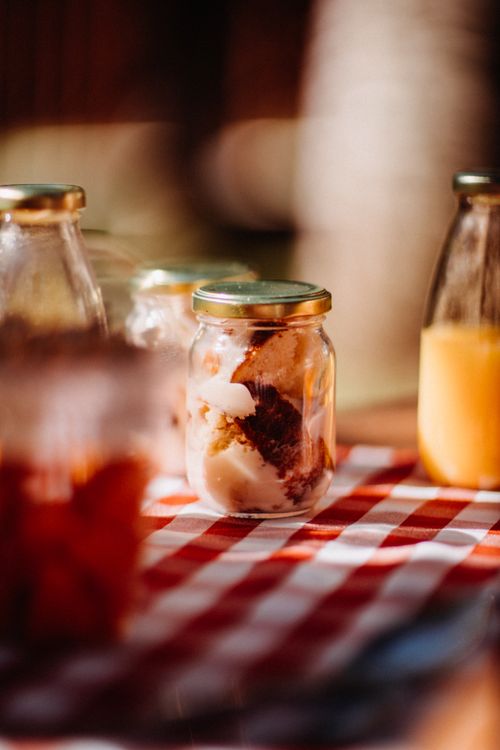 Free Glass jar filled with fruits served on checkered tablecloth with bottle of juice and dishware in sunny countryside on blurred background Stock Photo