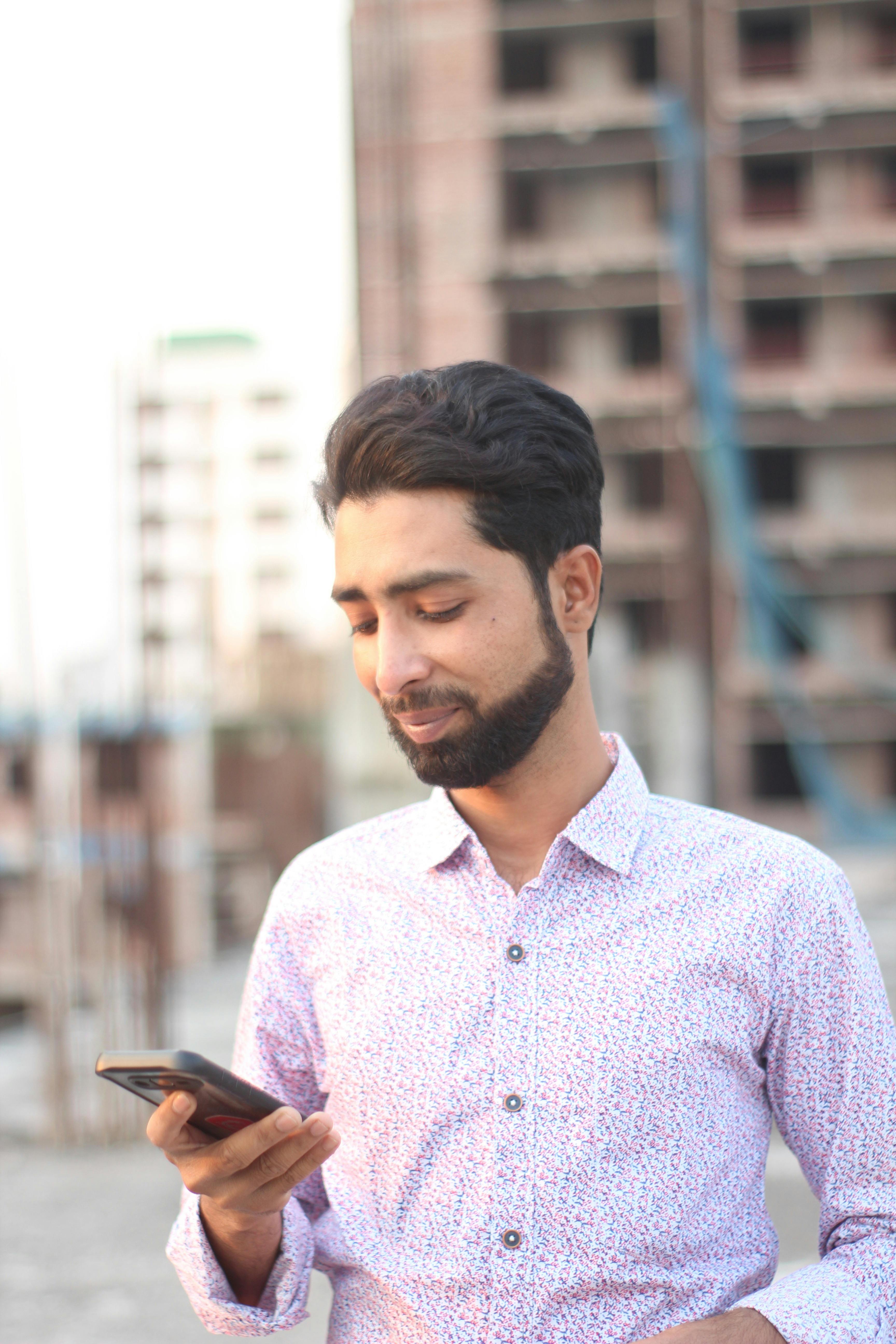 Young man using smartphone outdoors with urban background during daytime.
