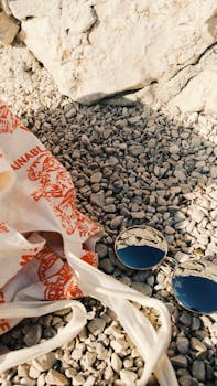 岩石海岸上，戴着太阳镜、拎着手提袋的极简主义海滩场景映照着晴朗的天空