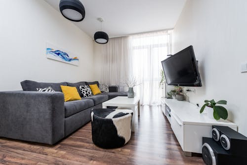 Comfortable gray sofa with yellow pillows placed in light living room in front of TV hanging on wall in modern apartment