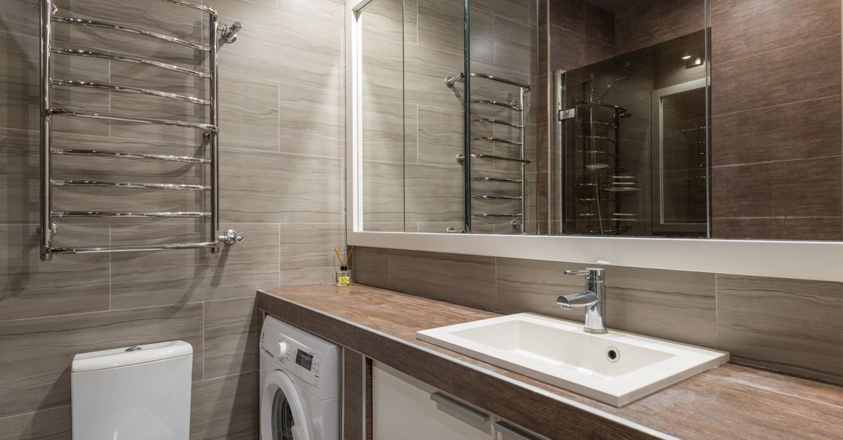 White ceramic toilet bowl and sink in contemporary bathroom with big mirror reflecting brown tiled walls