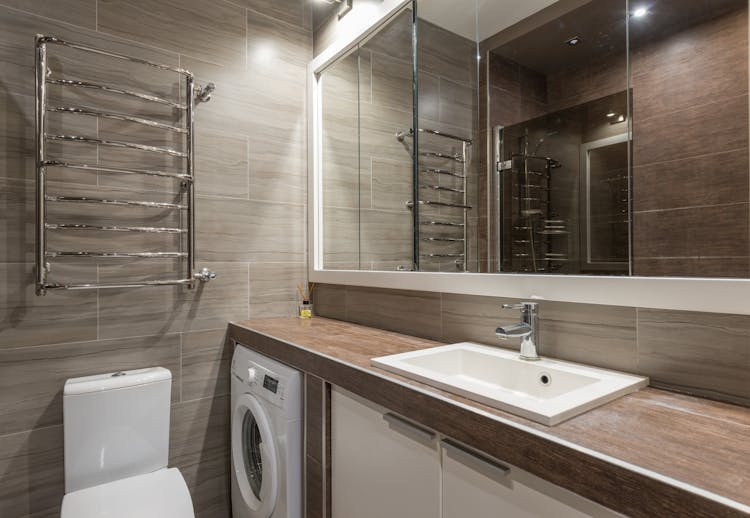 Interior Of Modern Bathroom With Big Mirror And Brown Tiled Wall