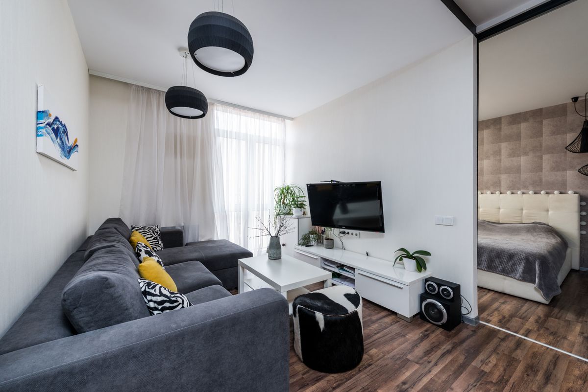 Sala pequena decorada com sofá cinza, rack branco, plantas e mesa compacta