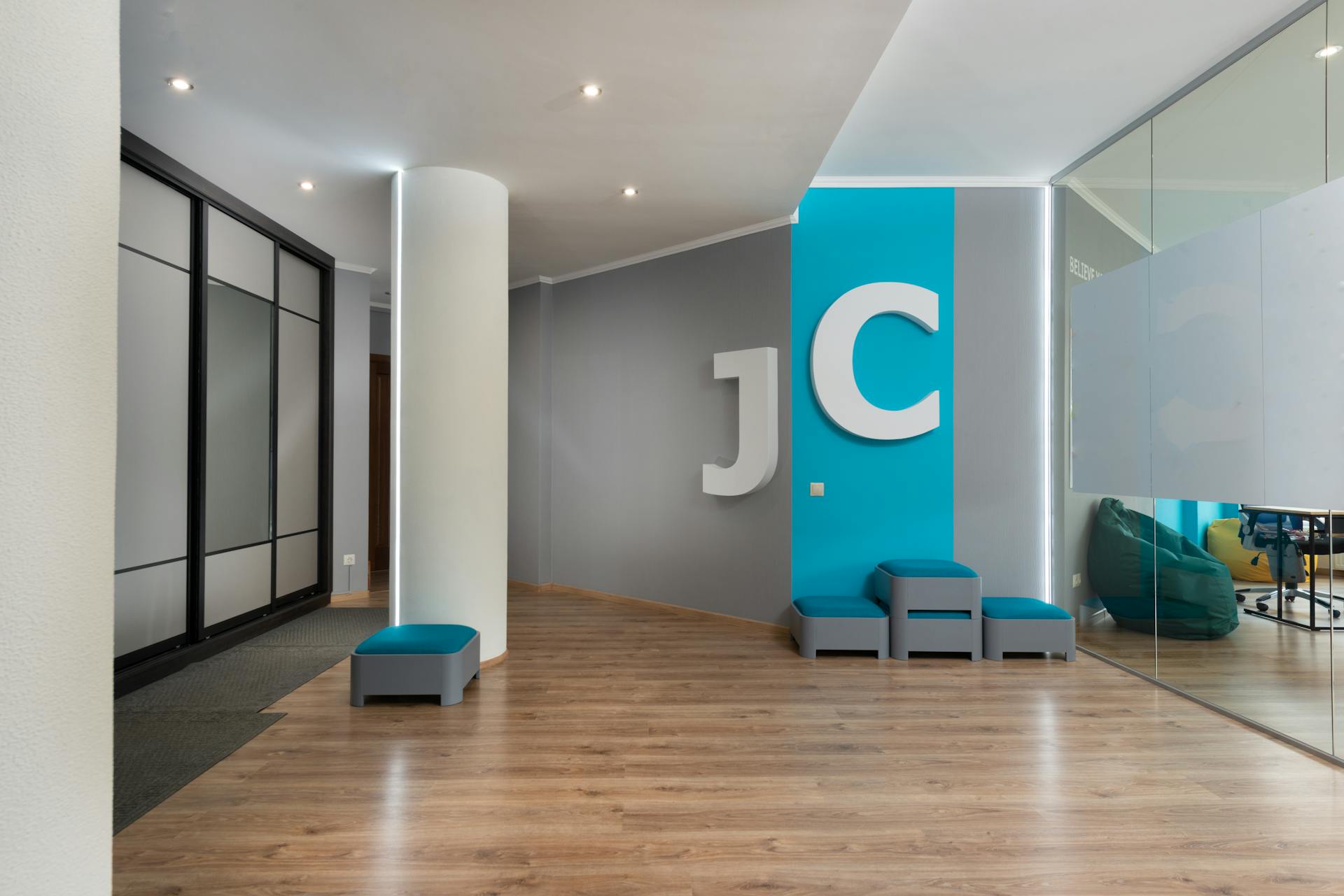 Comfortable poufs placed near wall with J and C letters in modern corridor with column near glass walls in contemporary business center