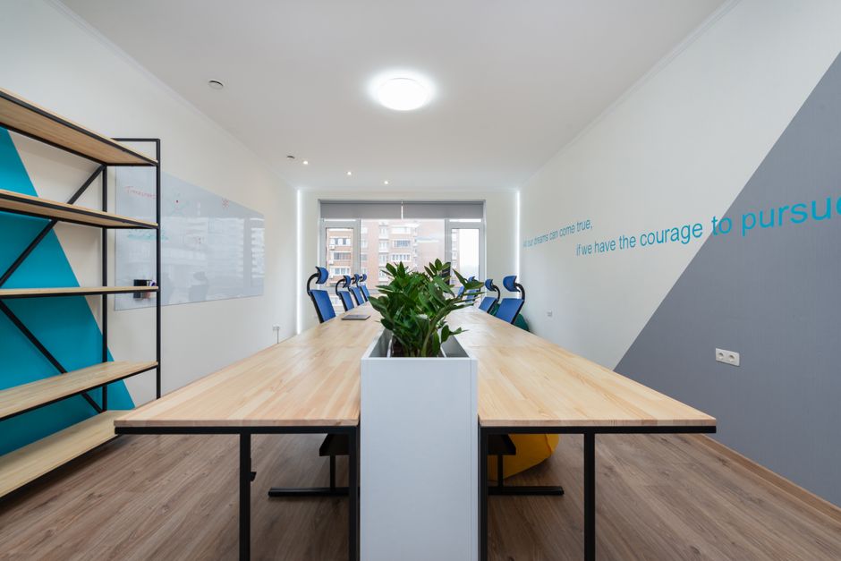Wooden table with green plants placed in light conference room with empty shelves and motivational inscription on wall in office building