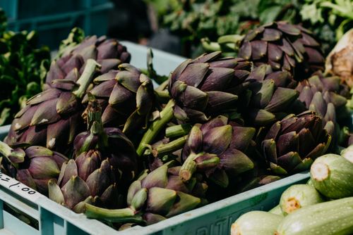 Free Close-up of fresh artichokes in a blue tray at an outdoor market. Stock Photo