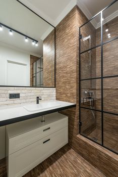 White cabinet under sink at wall with mirror near glass shower cabin in modern stylish bathroom with glowing lights in apartment