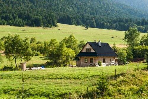 Free Scenic view of a wooden country house surrounded by lush green fields in Slovakia's countryside. Stock Photo