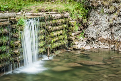 Waterfalls on Wooden Logs Near a Rocky Mountain