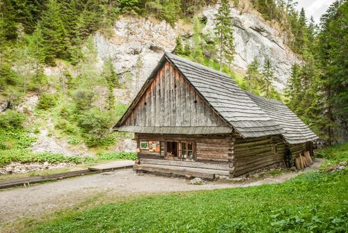 Free Charming wooden cabin nestled in lush green forest and rocky mountain landscape. Stock Photo
