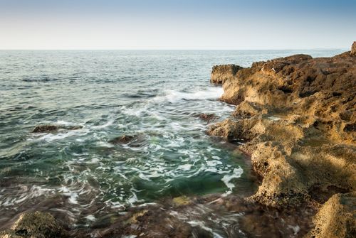 Free Waves crashing on a rugged rocky coastline under a clear sky, showcasing nature's beauty. Stock Photo