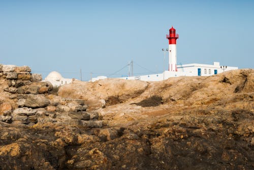 Free White and Red Lighthouse on Brown Rock Formation Under Blue Sky Stock Photo