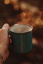 Crop anonymous person showing ceramic mug with steam from hot beverage in sunlight on blurred bokeh background
