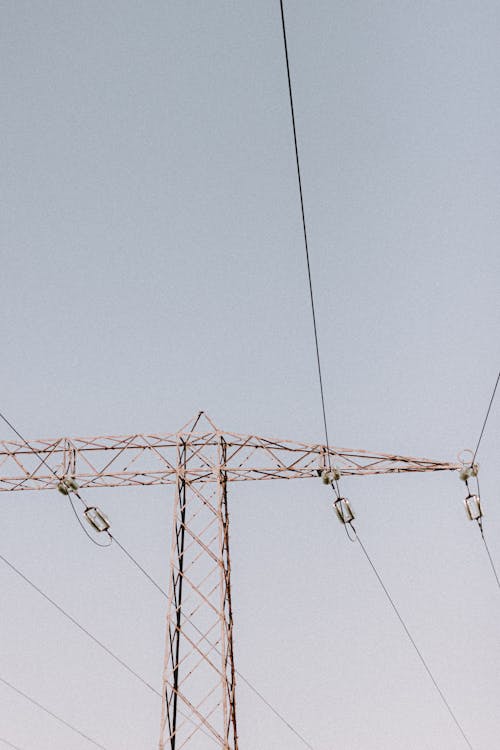 Low angle of metal transmission tower with wires under light grey sky in daytime