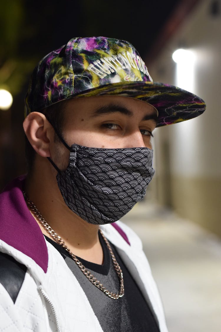 Trendy Man In Textile Mask And Chain Against Shiny Lights