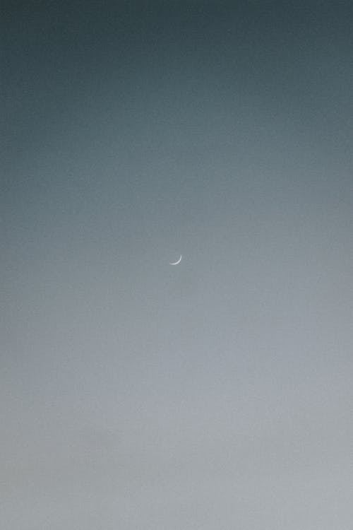 Low angle scenic view of wavy half moon in light gray sky in twilight