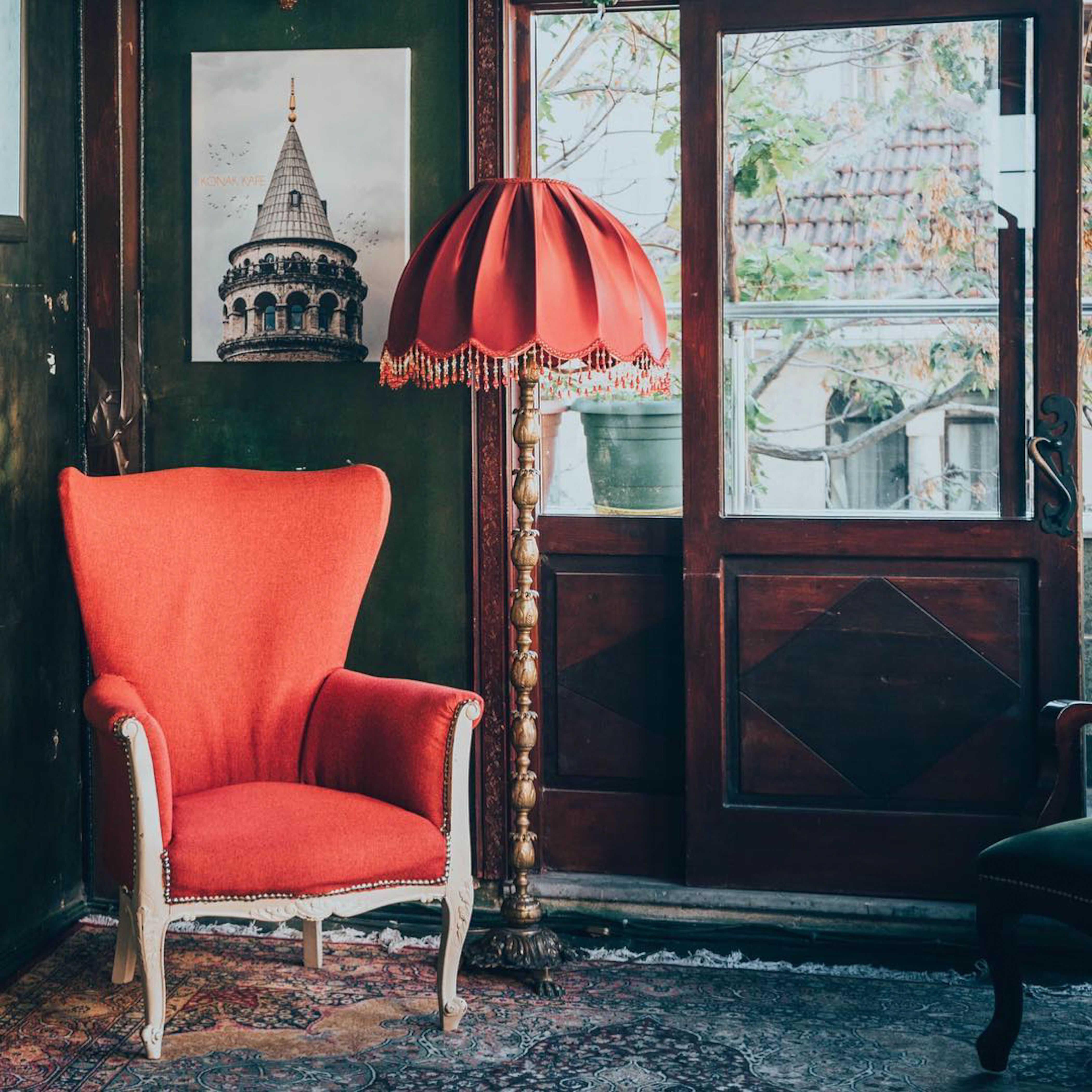 Cozy vintage interior featuring a red armchair and lamp with Galata Tower artwork as a backdrop.