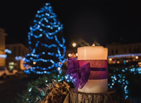 Close-up of candle with purple ribbon, Christmas tree lights in background, night celebration.