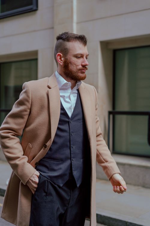 Free Bearded man in a camel coat and suit walking confidently in an urban setting. Stock Photo