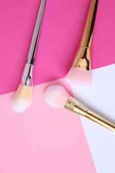 Minimalist display of makeup brushes with gold and silver handles on vibrant pink background.
