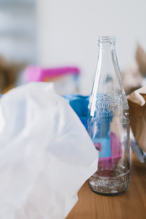 Glass bottle near plastic bag and paper for utilization